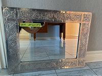 Front view of the rectangular mirror showing the full decorative ornate silver-tone frame with detailed embossed patterns and the reflective glass surface.