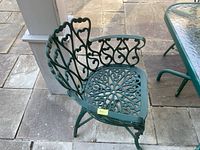 Front angle of one green cast-aluminum outdoor chair showing decorative openwork seat and backrest with armrests.