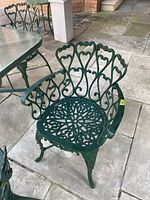 Front angled view of one green cast-aluminum outdoor chair beside a glass-top table