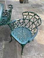 Front and side views of two green cast-aluminum patio chairs with decorative scroll and heart-shaped patterns.