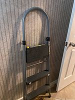 Frontal view of the 3-step metal folding ladder with curved top handle and black steps