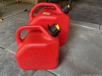 Two red gasoline cans, showing the front of both with the smaller can in front and larger behind.