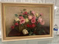 Full view of the framed antique still life oil painting depicting a basket of multicolored roses on a table.