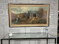 Full view of the framed landscape painting hung on a wall above a glass table with a water bottle for scale.