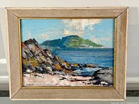 Full view of the framed oil painting showing seascape with rocky shore and island under blue sky.