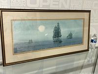 Wide view of framed watercolour painting showing tall ships on the sea with a light sky background and gold frame.