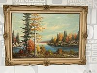 Full view of the framed landscape painting showing the river, trees with autumn foliage, and sky.