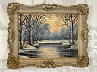 Framed full view of the oil painting showing a winter river landscape with trees and sunset sky.