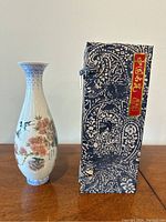 Photo showing the vase standing next to the original decorated box, highlighting the overall shape and size.