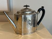 Front view showing octagonal body, wreath engraving, pierced border band, spout and black wooden handle