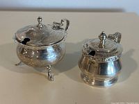 Two sterling silver pots side by side on neutral background