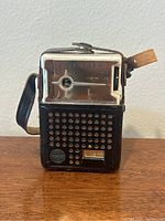 Front view of TAC 6TR transistor radio showing tuning dial, volume slider, perforated speaker grille, and leather strap.