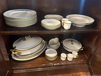 Full set displayed on wooden shelf showing stack of plates, cups, serving pieces with gold accents