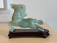 Side profile of the green jade carved horse figurine mounted on a dark wooden base showing glossy finish and flowing mane detail.