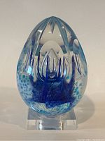 Front view of egg-shaped glass paperweight with blue internal pattern on clear lucite stand