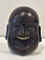 Front view of the larger carved wooden Laughing Buddha face sculpture showing detailed facial features and wood grain.