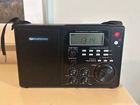 Front view of Grundig S450DLX portable radio showing speaker on left, digital display, control knobs and band selection buttons on front panel.