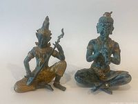 Pair of Thai bronze Buddha sculptures, one playing flute seated cross-legged, another playing stringed instrument seated with one leg bent, showing overall condition and detailing.