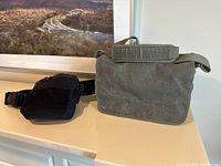 Overall front and side view of two camera bags: large olive green canvas shoulder bag (Retrospective 7) with visible wear crease marks, and black waist bag (Lens Changer 75) with mesh side panel, placed on shelf.