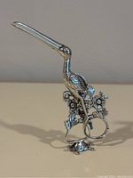 Front view of entire sugar nips showing stork figure atop floral base and tortoise support.