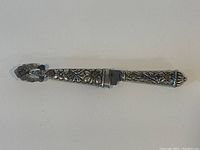 Top view of the silver handled cutting utensil fully sheathed, showing overall design and matching sheath featuring floral and leaf relief decoration.