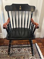 Front view of vintage black and brown wooden armchair with U of T gold crest on headrest, showing condition and design details.