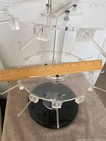 Clear view of the acrylic turntable jewelry display stand showing its arms, one circular tier, and black base with ruler for scale.