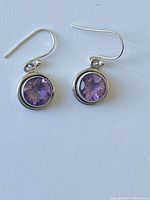 Pair of sterling silver earrings with round faceted amethyst stones and hook backs.