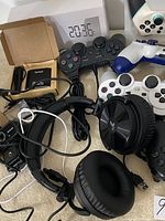 Image showing multiple gaming controllers including PlayStation and Xbox style along with a black USB wired headset with microphone and ear cushions.