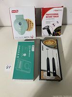 Photo displaying boxed Dash Mini Maker Waffle, Professional Butane Torch, Baliir Digital Mini Scale, and Datoli Electric Milk Frother in original packaging