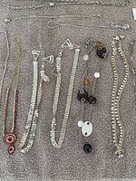 Top view of 7 necklaces laid out on a beige towel showing variety of styles including beaded pendants, rhinestones, chain link, and multi-beaded designs.