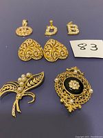 Top view of vintage costume jewelry including heart-shaped earrings, letter pendants, and two brooches