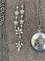 Silver-tone necklace with crystal flower motifs and a round pendant with ornate detailing on textured fabric background