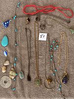 Lot of vintage necklaces and stones laid out on surface showing variety of stone pendants and bead necklaces.