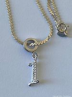 Close-up image showing the silver chain and the number '1' charm with small stones.
