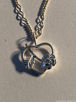 Close-up image of the pendant showing the heart shape with a rose flower and leaf detail.