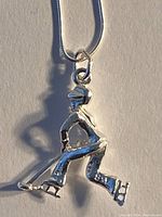 Pendant shaped like a hockey player wearing skates, holding a hockey stick. Pendant attached to a silver chain.