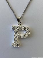 Close-up photo of the pendant showing a letter 'P' made of sterling silver, encrusted with clear round-cut stones.
