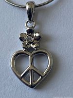 Close-up of sterling silver necklace pendant shaped as a heart with peace sign and a flower with a gem.