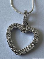 Heart-shaped sterling silver pendant necklace with multiple small clear stones set all around the pendant, shown from two slightly different angles.