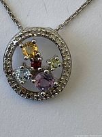 Close-up of circular pendant with multiple colored stones in setting.