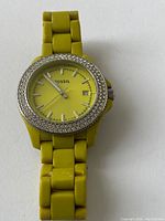 Front view of yellow Fossil watch showing dial, rhinestone bezel, and linked strap.