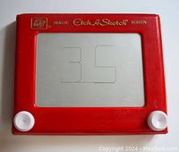 Front view of original red plastic frame Etch A Sketch showing screen with faint drawing and two white knobs