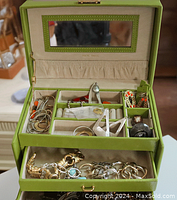Open green vintage jewelry box showing assorted jewelry in compartments and drawers.