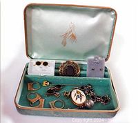 Vintage jewelry box with assortment of rings, brooches, earrings, bracelet, and pendant displayed inside on velvet lining.