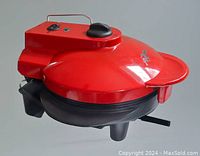 Red Xpress Redi-Set-Go electric grill with control dial and power indicator light on top. The unit is on legs with visible cord and power switch on side.