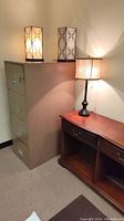 Photo shows metal filing cabinet, wooden credenza, and three table lamps illuminated on top of the furniture.