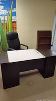 Photo showing black office desk, black office chair, and wooden magazine rack in office setting.