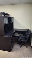 Side view of the L-shaped dark wood office desk with hutch, showing compartments and the black leather office chair positioned in front.