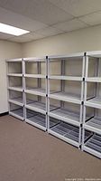 Four white plastic shelving units, each with four ventilated shelves, arranged against a wall in an office setting.